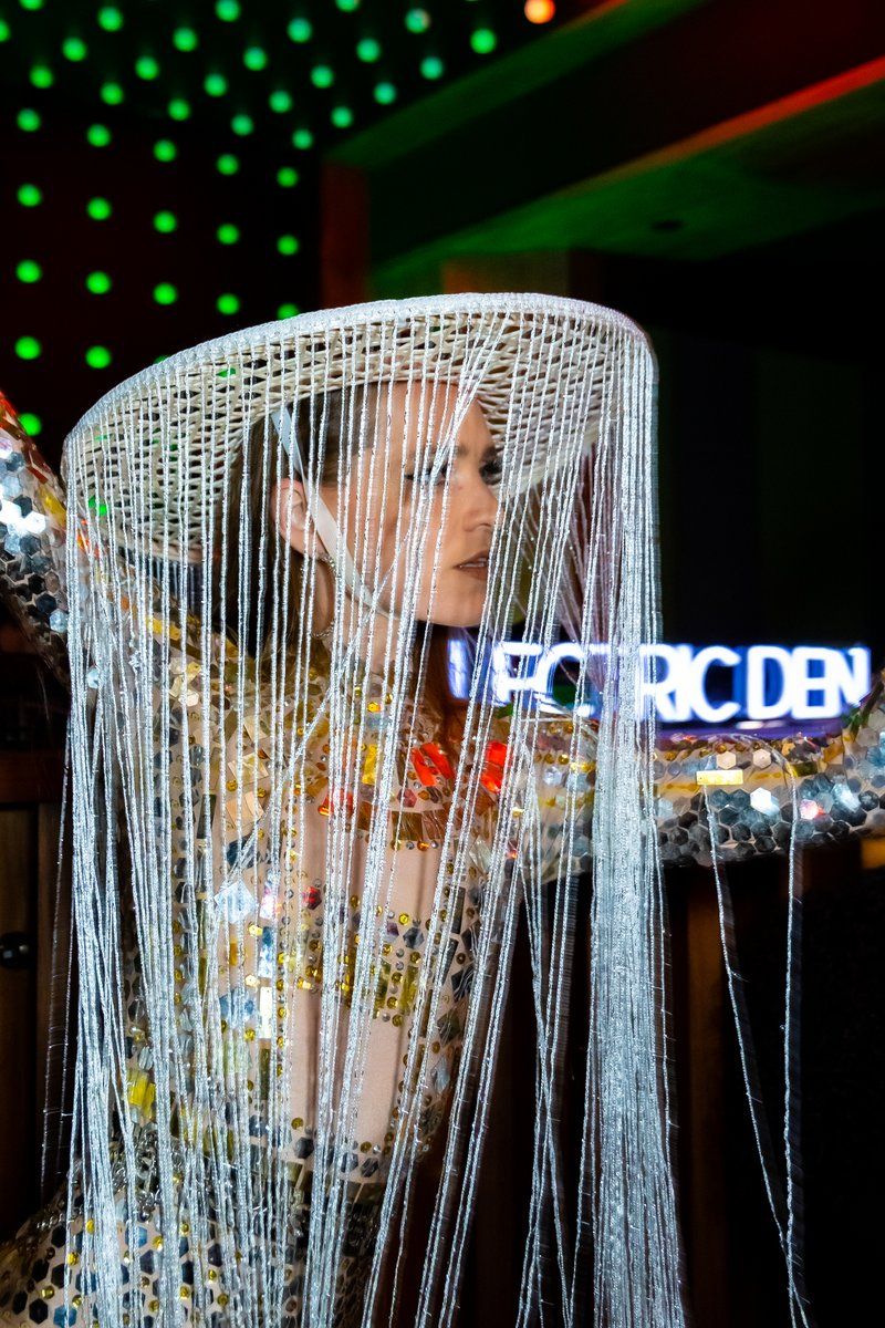 Guest in a beaded fringe headpiece under the Electric Den neon sign at Jolene Sound Room