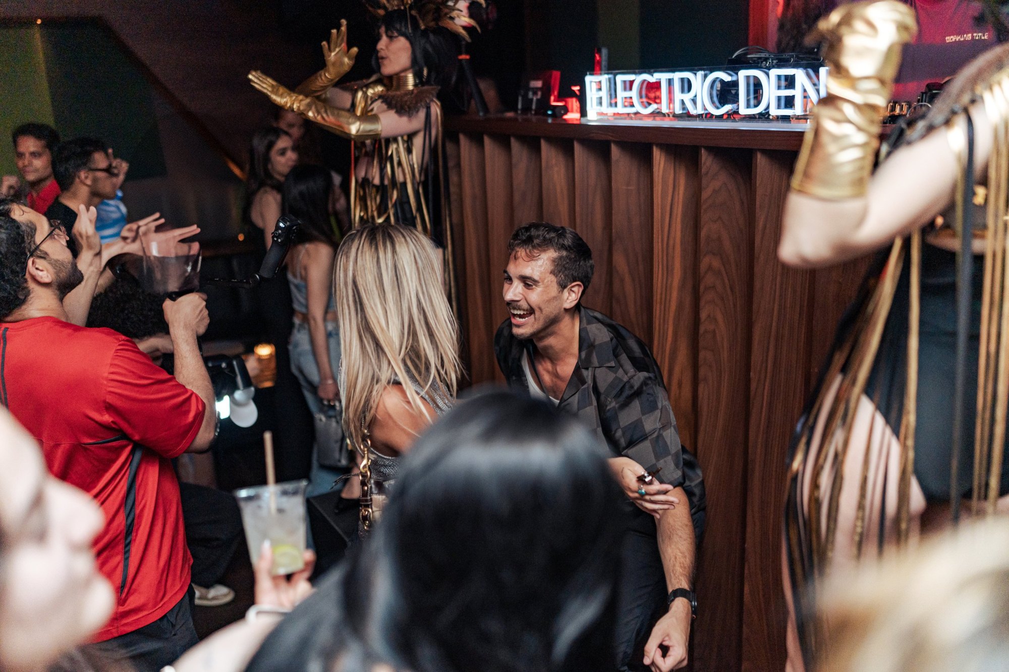 A performer in gold dancing on the bar beside the Electric Den sign at Jolene Sound Room