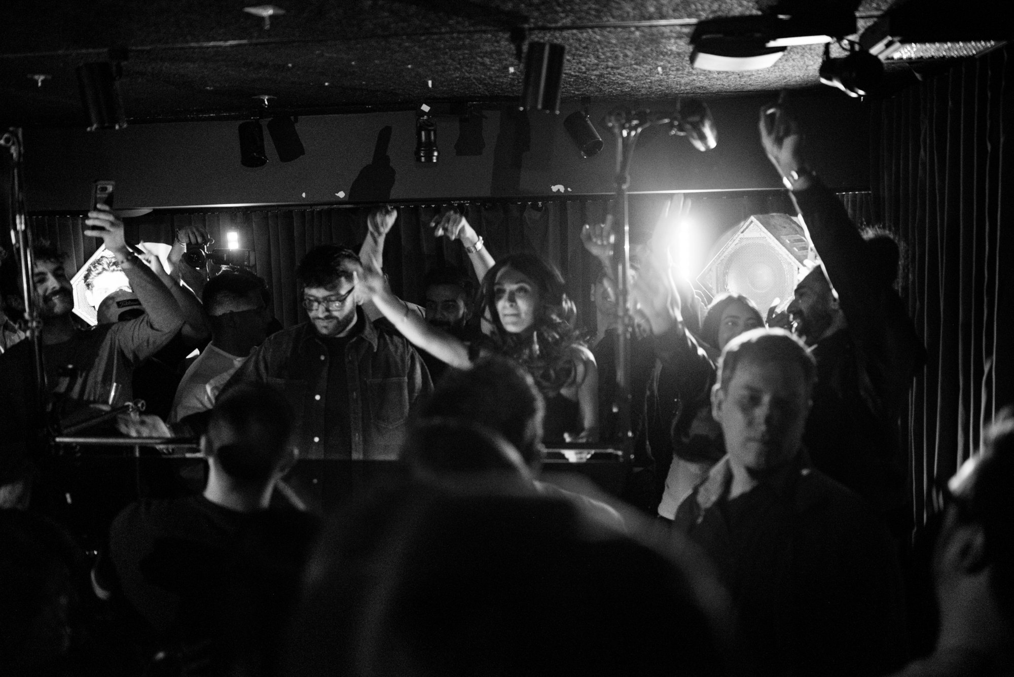 Black and white photo of the booth and crowd with hands up in the Blue Room at Public Hotel